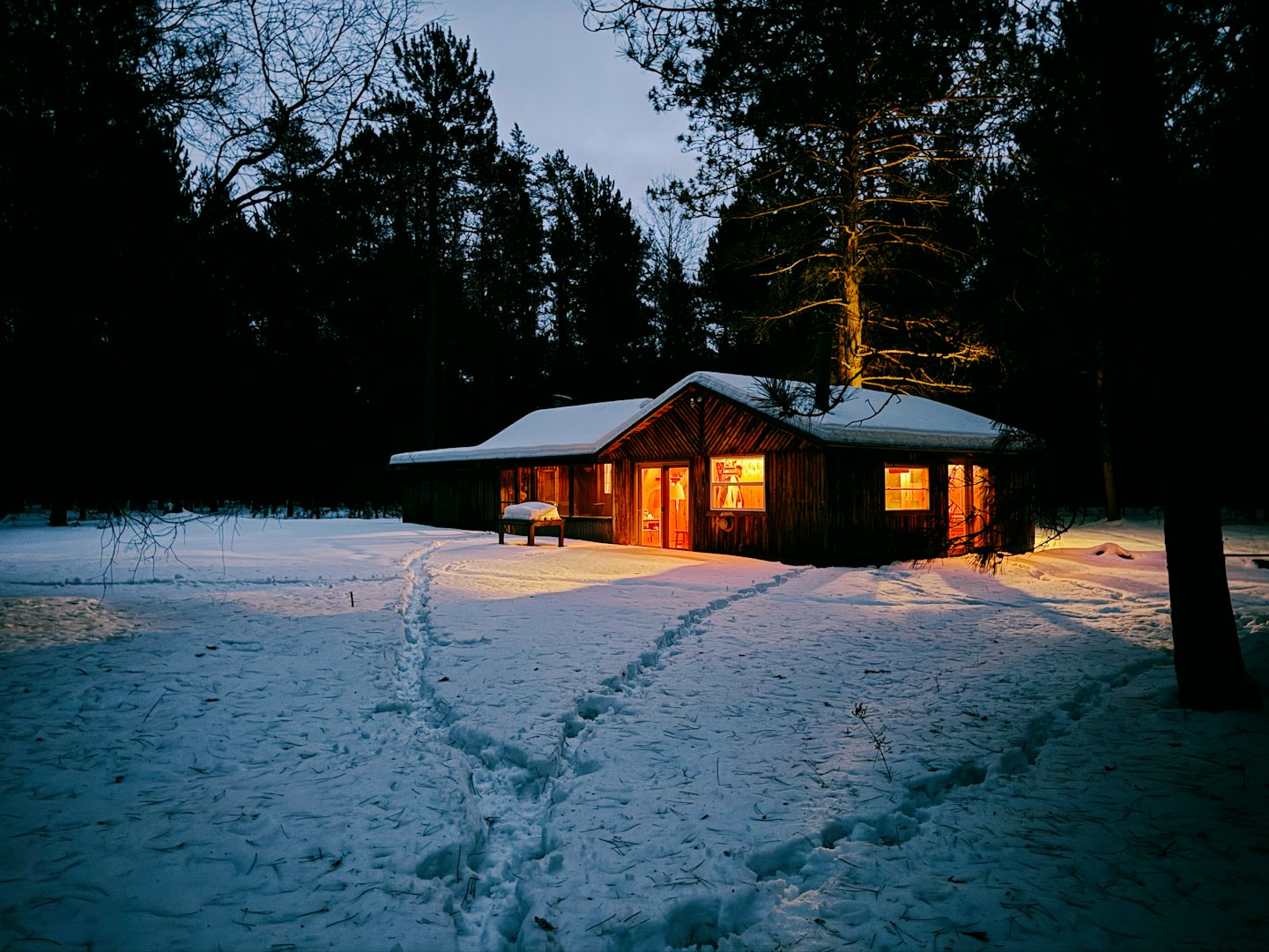 Snöiga fotspår leder till en glödande stuga i skogen.