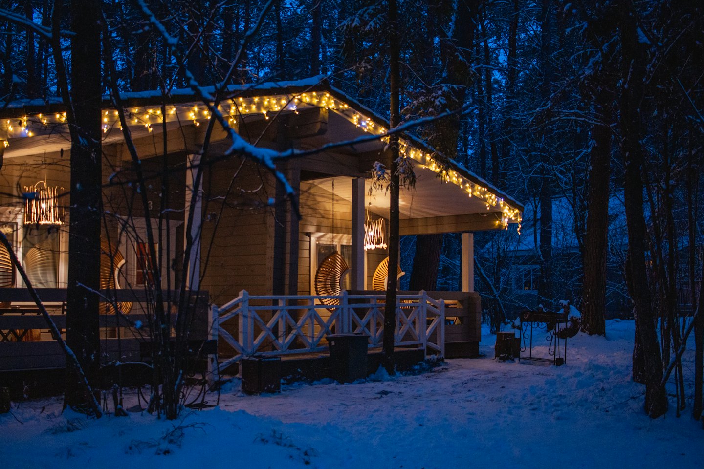 En snötäckt stuga lyser med ljus i en vinterskog.